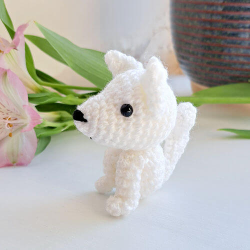 A cute little artic wolf pup crochet art figure looking left sitting on a window sill