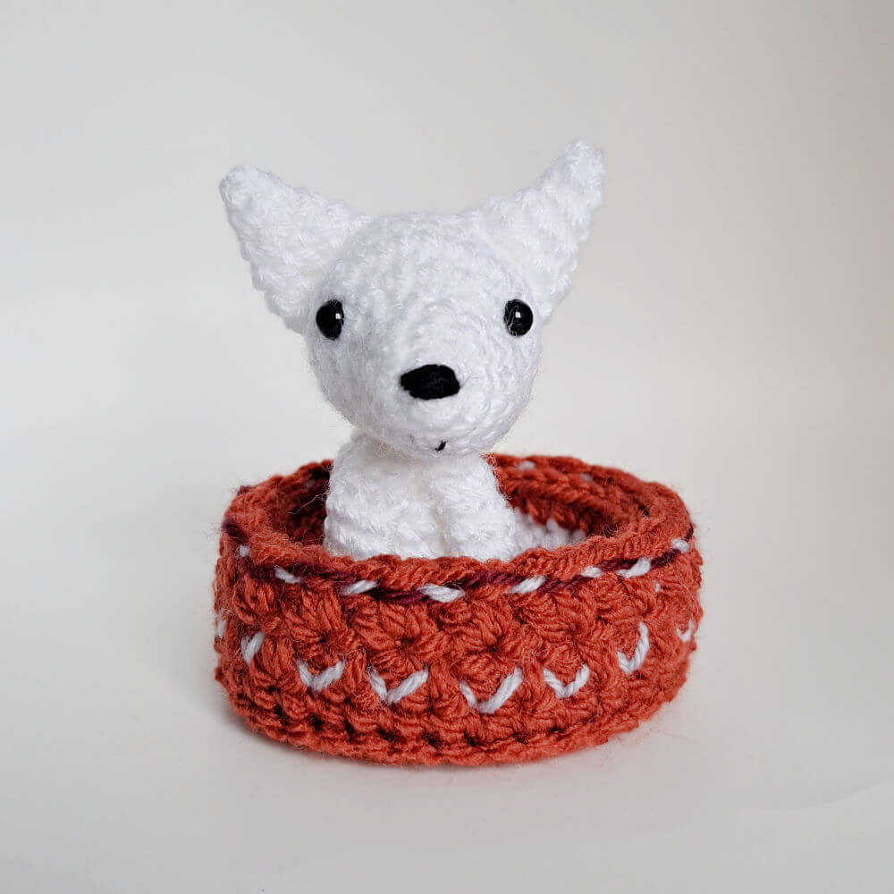 A cute little artic wolf pup crochet art figure sitting in her embroidered basket