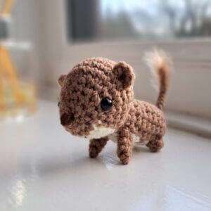 A cute weasel ornament, a weasel crochet figure on a window sill.