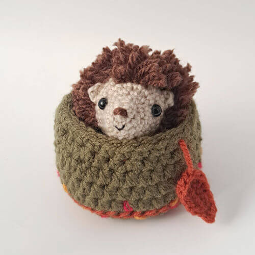 A cute little hedgehog crochet art figure peeping out of its little embroidered nest