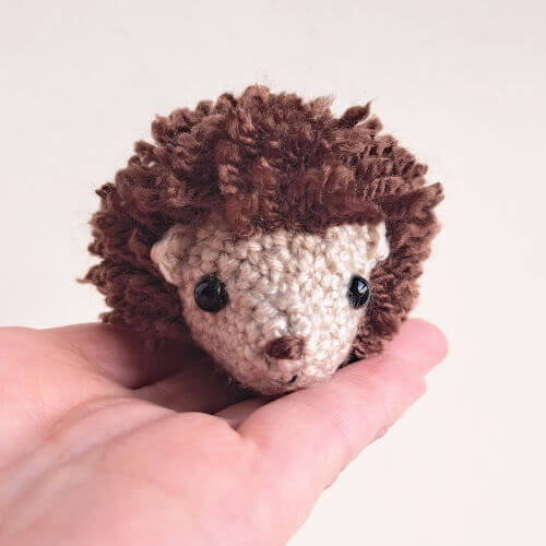 An adorable hedgehog textile art figure sitting in the palm of a hand.