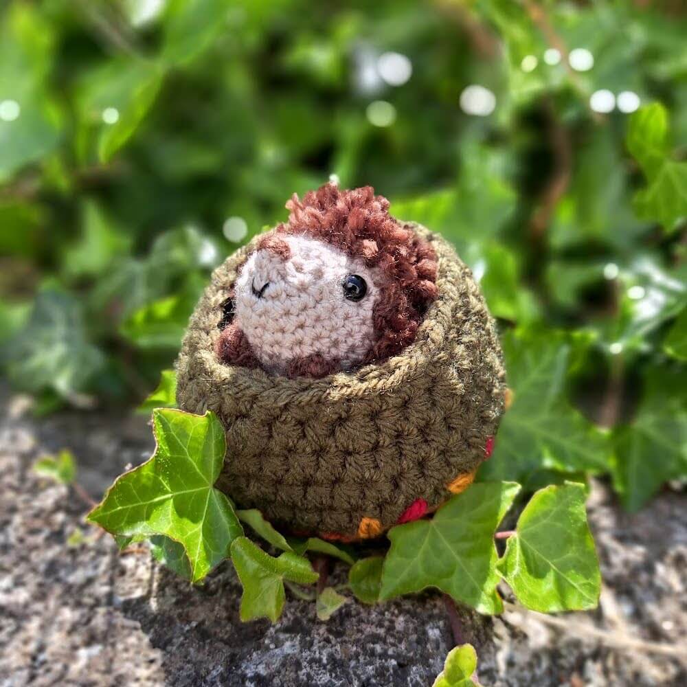A cute little hedgehog crochet art figure peeping out of his little nest
