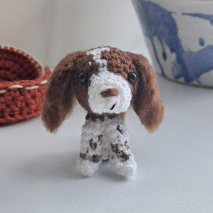 A cute little springer spaniel gift crochet figure sitting on a window ledge by a plant pot
