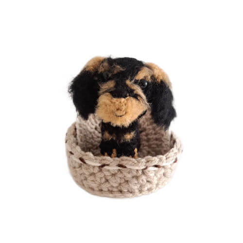 A wire-haired dachshund crochet art figure sitting in a crochet basket