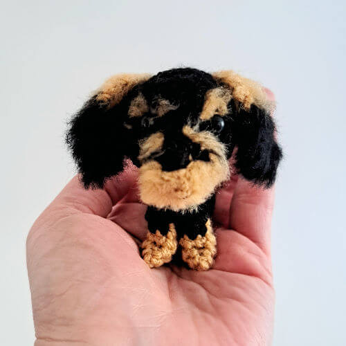 An adorable little wire-haired dachshund crochet art figure sitting on the palm of a hand