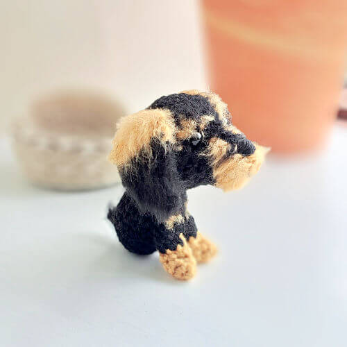 A cute little wire-haired dachshund crochet art figure sitting on a window ledge looking out of the window