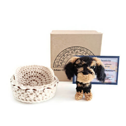 A gorgeous little wire-haired dachshund crochet art figure sitting with a gift box, crochet basket and provenance card