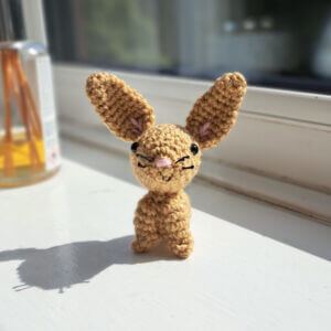 An adorable little folk art crochet brown rabbit ornament sitting on a sunny window sill