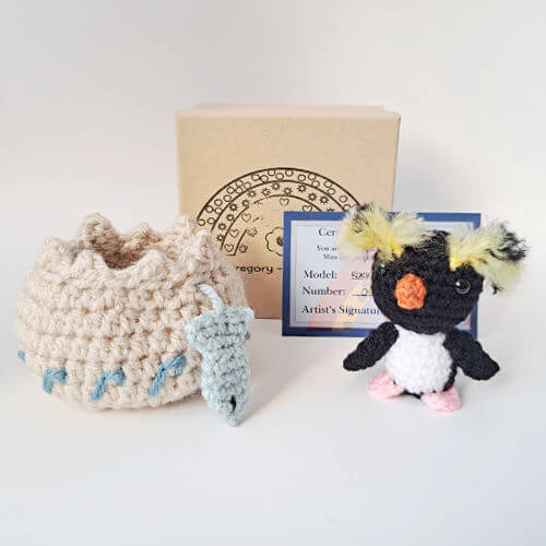 A rockhopper penguin crochet art figure with embroidered nest, fish, certificate of authenticity and gift box