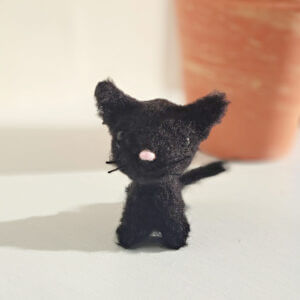 Cute fluffy black cat ornament sitting on a window sill with a plant pot in the background