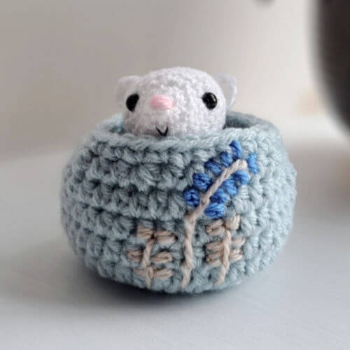 Ermine crochet art figure peeking out of her cozy embroidered nest