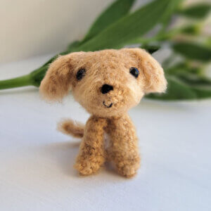 Brown cavapoo gift crochet art figure sitting on a window sill with a flower in the background