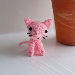 Pink cat ornament, a cute little crochet pink cat sitting on a window ledge near a plant pot